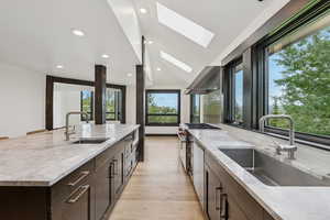 Kitchen with a skylight, wall chimney exhaust hood, plenty of natural light, dark brown cabinetry, and recessed lighting