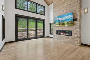Unfurnished living room featuring high vaulted ceiling, a stone fireplace, and wood finished floors
