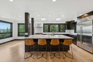 Kitchen featuring built in fridge, wall chimney range hood, tasteful backsplash, light wood-type flooring, and recessed lighting