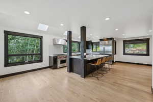 Kitchen with premium appliances, wall chimney range hood, a skylight, a breakfast bar, and healthy amount of natural light