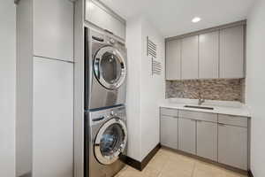 Laundry area featuring estacked washer and dryer, cabinet space, recessed lighting, and light tile patterned floors
