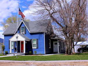 Bungalow-style home with a shingled roof, a front yard, and covered porch