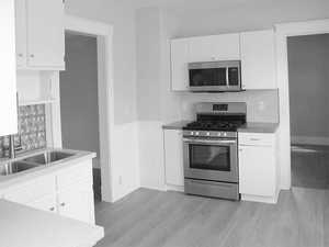 Kitchen with appliances with stainless steel finishes, light wood finished floors, white cabinets, and a wainscoted wall