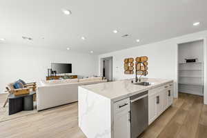 Kitchen featuring dishwasher, white cabinetry, light wood-type flooring, light stone counters, and a kitchen island with sink. pic of model home of same floor plan, actual home may vary slightly on flooring, colors, cabinets, etc.