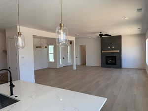 Kitchen featuring light wood-style flooring, ceiling fan, a textured ceiling, a large fireplace, and light stone counters