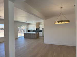 Kitchen featuring light wood-type flooring, wall chimney exhaust hood, decorative backsplash, white cabinets, and recessed lighting