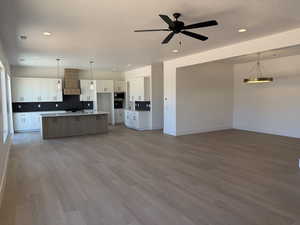 Kitchen featuring premium range hood, stainless steel microwave, open floor plan, white cabinetry, and decorative backsplash