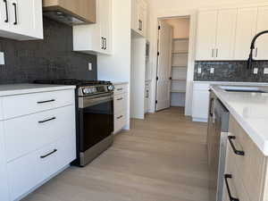 Kitchen featuring stainless steel appliances, extractor fan, light wood finished floors, backsplash, and white cabinets
