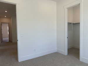 Unfurnished bedroom with light carpet, a walk in closet, recessed lighting, and a closet