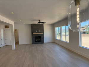 Unfurnished living room featuring ceiling fan, a textured ceiling, light wood-type flooring, a large fireplace, and recessed lighting
