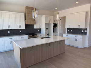 Kitchen featuring appliances with stainless steel finishes, light wood-style floors, light stone countertops, backsplash, and a kitchen island with sink