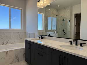 Full bath featuring healthy amount of natural light, a marble finish shower, a bath, and double vanity