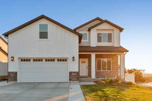 View of front of home featuring driveway, board and batten siding, a front lawn, and stone siding