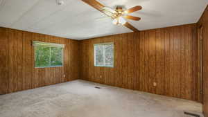 Primary bedroom featuring wooden walls, a ceiling fan, and an en suite bathroom