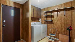 Washroom with separate washer and dryer, light wood-style flooring, wood walls, and cabinet space