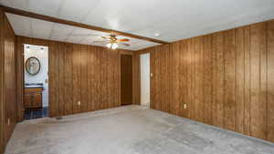 Primary bedroom featuring a ceiling fan, wooden walls, and an en suite bathroom