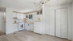 Kitchen with white appliances, range hood, ceiling fan, light countertops, and light wood finished floors