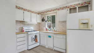 Kitchen featuring white appliances, range hood, light countertops, white cabinetry, and light wood-style floors