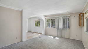 Carpeted living room with arched walkways and ornamental molding
