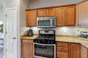 Kitchen featuring appliances with stainless steel finishes, brown cabinetry, and light stone counters