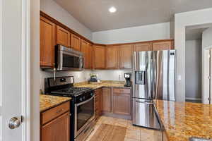 Kitchen featuring stainless steel appliances, brown cabinets, light stone counters, light tile patterned floors, and recessed lighting