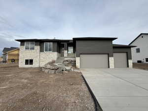 View of front facade featuring a garage, driveway, and stone siding