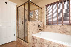 Full bath featuring a garden tub, a shower stall, and stone finish floors