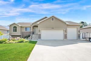 Ranch-style house with stucco siding, stone siding, an attached garage, a front yard, and driveway