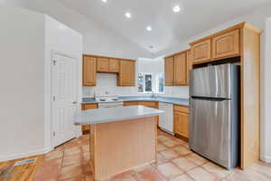 Kitchen featuring white appliances, lofted ceiling, light countertops, a center island, and recessed lighting