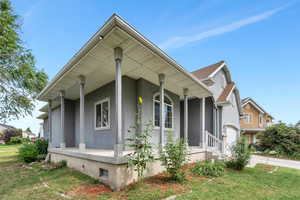 View of side of property with stucco siding, covered porch, driveway, and a yard