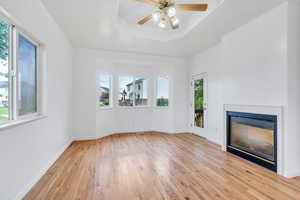 Unfurnished living room with plenty of natural light, light wood-type flooring, a glass covered fireplace, and a ceiling fan