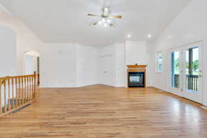Unfurnished living room featuring light wood-style flooring, a ceiling fan, a glass covered fireplace, arched walkways, and recessed lighting