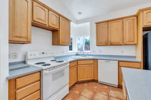 Kitchen featuring white appliances, light countertops, vaulted ceiling, light brown cabinets, and light tile patterned floors