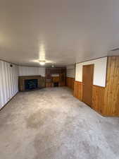 Unfurnished living room with wooden walls, carpet, wainscoting, and a fireplace