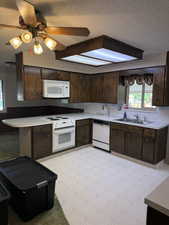 Kitchen featuring white appliances, a textured ceiling, dark brown cabinetry, light countertops, and light flooring