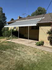 Back of property with brick siding, a lawn, a chimney, roof with shingles, and a patio area