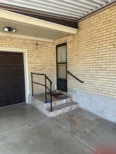 Property entrance featuring a garage, brick siding, and a porch