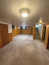 Below grade area featuring wood walls, stairway, and light colored carpet