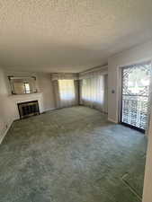 Unfurnished living room with a textured ceiling, plenty of natural light, a glass covered fireplace, and carpet floors
