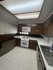 Kitchen featuring white appliances, light flooring, dark brown cabinets, a wainscoted wall, and light countertops