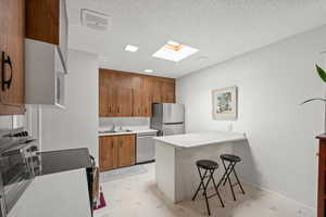 Kitchen featuring appliances with stainless steel finishes, a skylight, a peninsula