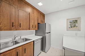 Kitchen with appliances with stainless steel finishes, brown cabinets, light countertops, and a textured ceiling