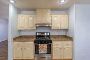 Kitchen featuring stainless steel range with gas cooktop, under cabinet range hood, dark countertops, and cream cabinetry