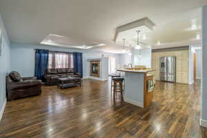 Living room featuring a tray ceiling, dark wood-style flooring, and a glass covered fireplace