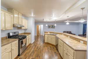 Kitchen featuring appliances with stainless steel finishes, cream cabinetry, under cabinet range hood, dark wood-style floors, and open floor plan