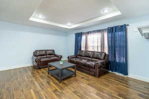 Living room with a tray ceiling, dark wood-style floors, and recessed lighting