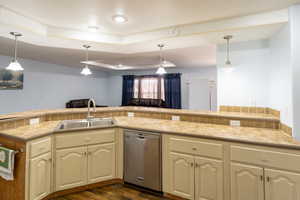 Kitchen with dishwasher, a tray ceiling, cream cabinets, light countertops, and pendant lighting