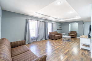Living room with a tray ceiling, arched walkways, hardwood / wood-style flooring, and recessed lighting