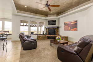 Living room with a tray ceiling, ceiling fan, light tile patterned floors, and a stone fireplace