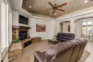 Living area with a raised ceiling, arched walkways, ceiling fan, a fireplace, and recessed lighting